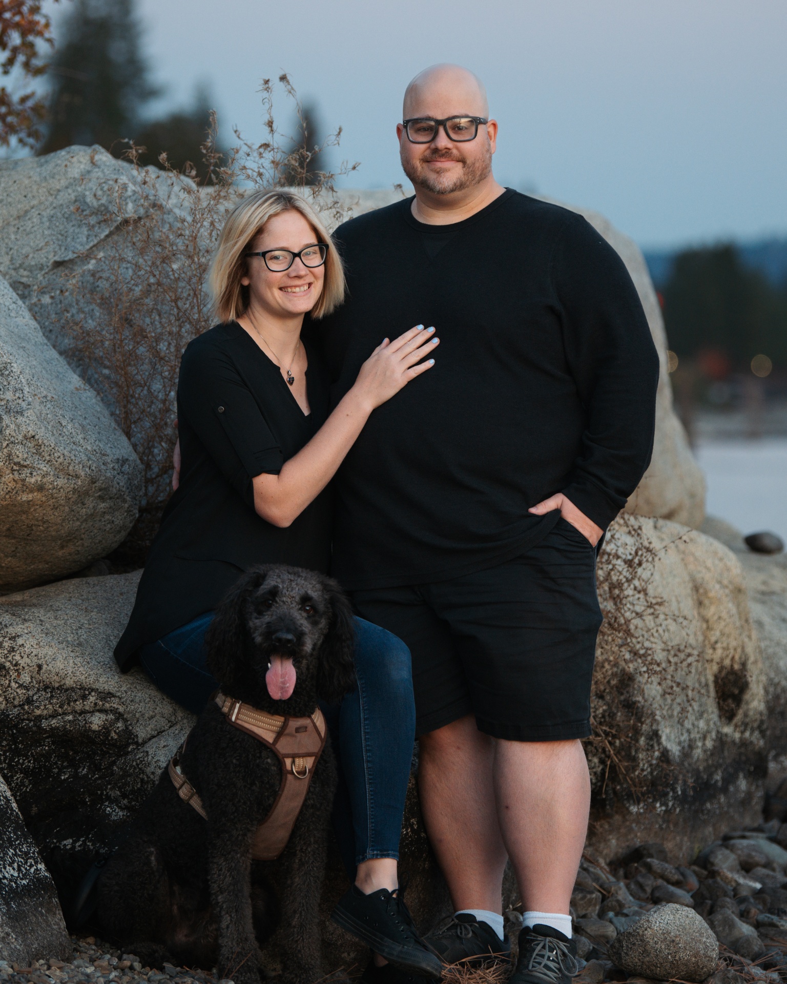 A man and woman posing with their dog on a rock.