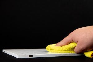 A hand wiping a computer screen with a yellow cloth.