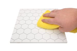 A person cleaning a hexagon tile with a yellow sponge.