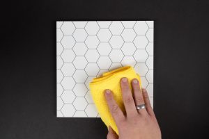 A person cleaning a hexagon tile with a yellow cloth.