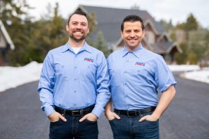 Two men in blue shirts standing in front of a house.