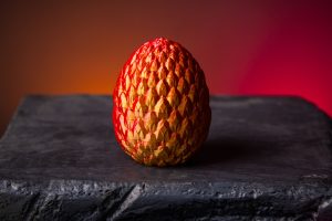 A red and yellow egg sits on top of a rock.
