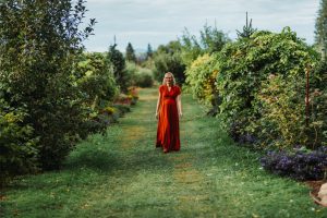 A woman in a red dress walking through an orchard.