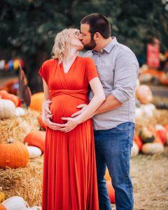 A pregnant couple kissing in front of pumpkins.