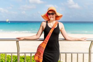 A woman in a black dress and orange hat standing on a railing near the beach.