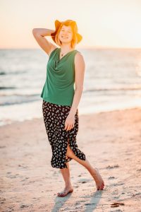 A woman wearing a green hat and polka dot skirt on the beach.