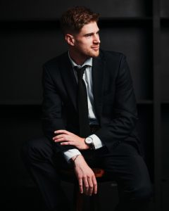 A man in a suit sitting on a stool.