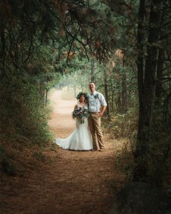 A bride and groom standing on a path in the woods.