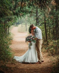 A bride and groom kissing on a path in the woods.