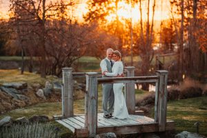 A bride and groom standing on a bridge at sunset.