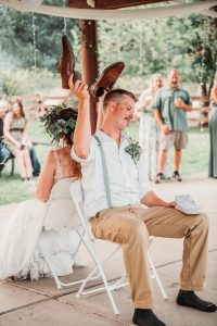 A bride and groom are holding their shoes up in the air during their wedding ceremony.