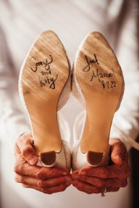 A bride holds up her wedding shoes with writing on them.